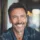 Homme souriant avec barbe et veste en jean.