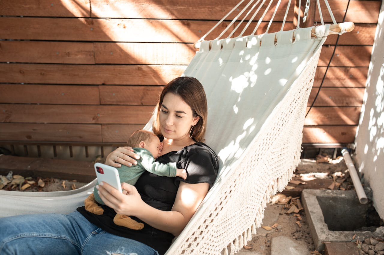 A woman relaxes in a hammock with her baby, enjoying a peaceful outdoor afternoon.